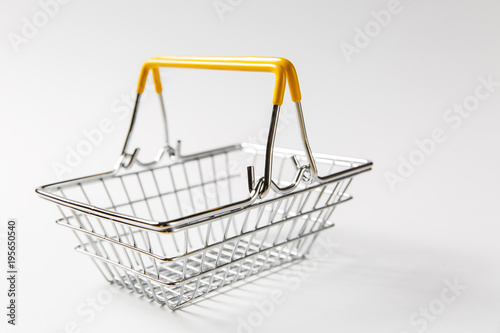 Close up of metal grocery basket for shopping in supermarket with yellow plastic elements on handle isolated on white background. Concept of shopping. Copy space for advertisement photo