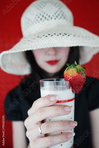 Mujer joven sosteniendo un vaso de leche con fresas  photo