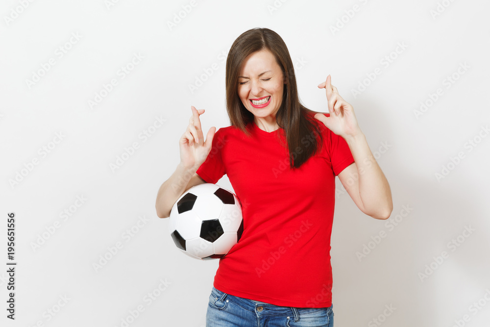 European young woman football fan or player in red uniform keep fingers crossed hold soccer ball isolated on white background. Sport play football lifestyle concept. Wait for special moment. Make wish