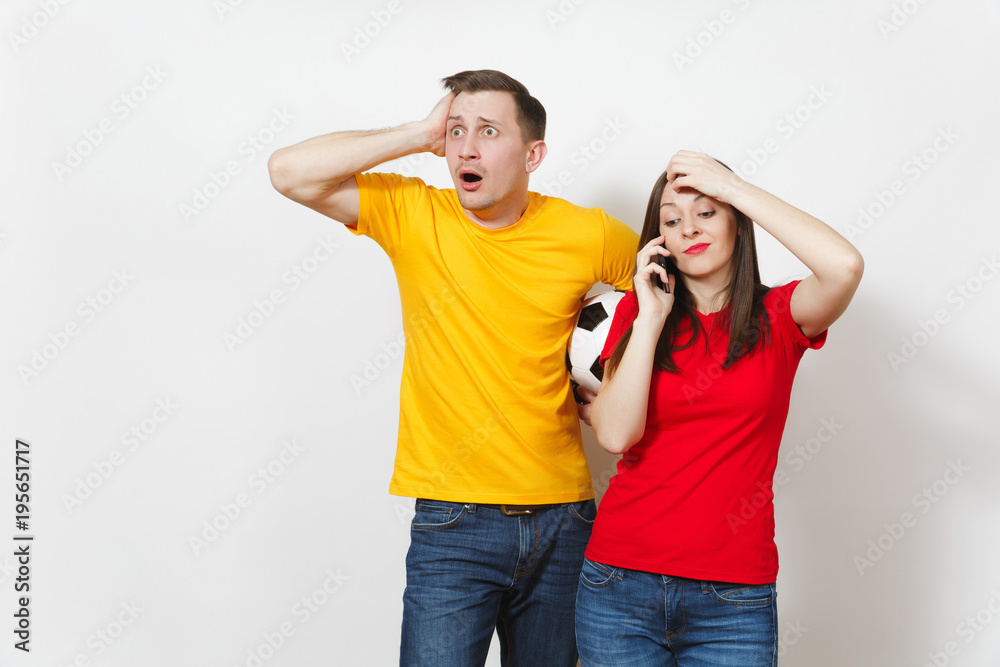 Fun engaged young man, indifferent woman talking on mobile phone, football fans cheer up support team with soccer ball isolated on white background. Sport, couple, family leisure, lifestyle concept. Fun engaged young man, indifferent woman talking on mobile phone, football fans cheer up support team with soccer ball isolated on white background. Sport, couple, family leisure, lifestyle concept.