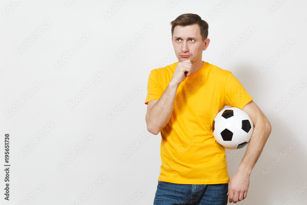 Inspired young pensive European man, fan or player in yellow uniform hold soccer ball, cheer favorite football team isolated on white background. Sport, play football, healthy lifestyle concept.