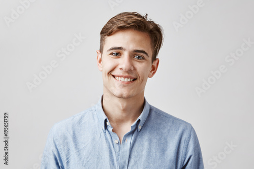 Cute boy with brown hair and beautiful smile standing next to the wall. His birthday is today so coworkers made surprise party. Guy looks happy he did not expected they will remember. photo