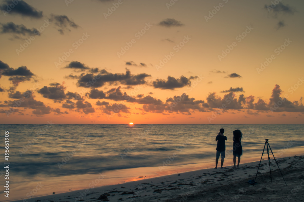 Two young people at the beach taking pictures at golden hour as the sun rises.