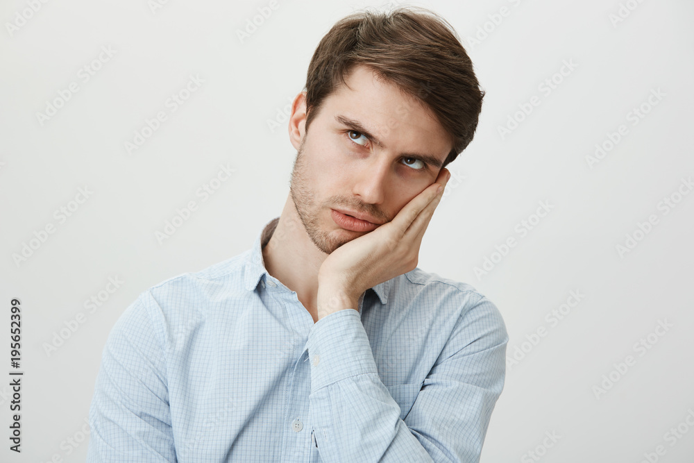 When will this hell over. Portrait of bothered and bored attractive young man in shirt leaning on palm and looking up as if checking time on clock, frowning and being displeased of wasting time When will this hell over. Portrait of bothered and bored attractive young man in shirt leaning on palm and looking up as if checking time on clock, frowning and being displeased of wasting time