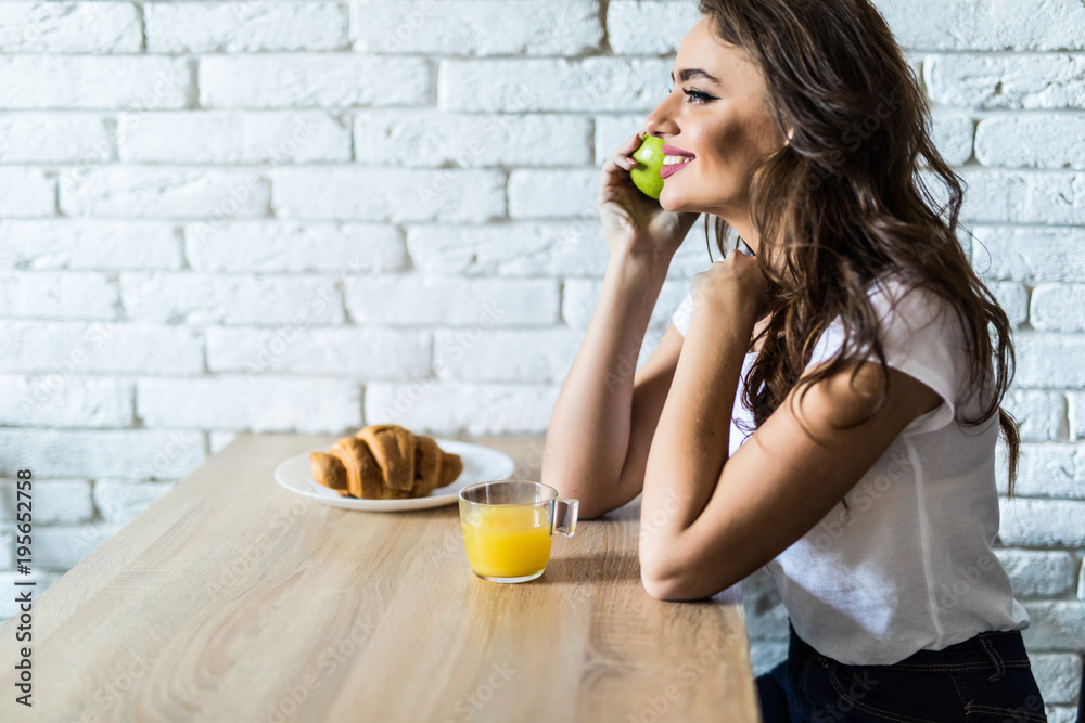 Young woman sitting at breakfast holding green apple, smiling at camera in the morning Young woman sitting at breakfast holding green apple, smiling at camera in the morning