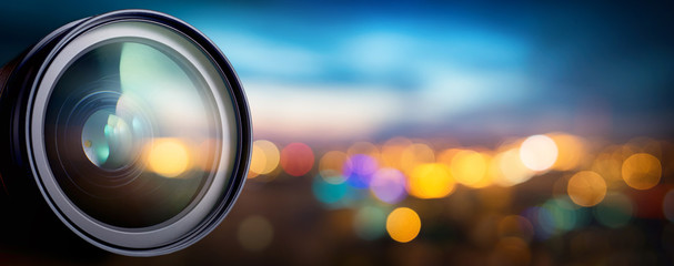 Camera lens with lense reflections on blur night city. Media and technology concept background. 