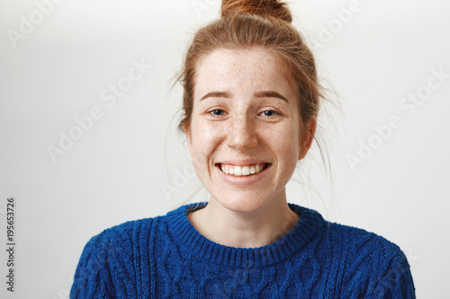 Close-up portrait of good-looking girl with freckles and natural red hair smiling nervously and chuckling, talking with new company, feeling shy, standing over gray background, trying to find friends