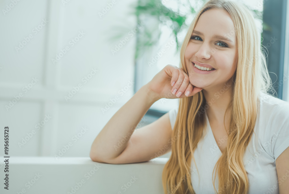 Close up Portrait of a beautiful smiling young blond woman sitting at home on a sofa and resting or relaxing.