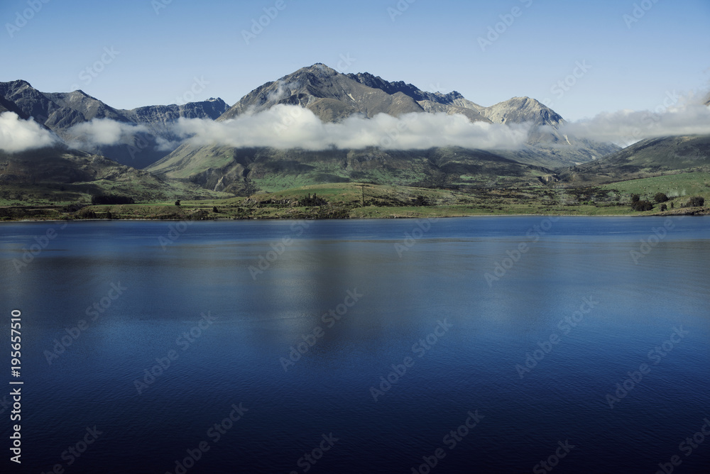 Paisaje de montañas con picos nevados y nubes. Las montañas se reflejan en un lago. Escena diurna, cielo azul y despejado. Nueva Zelanda.