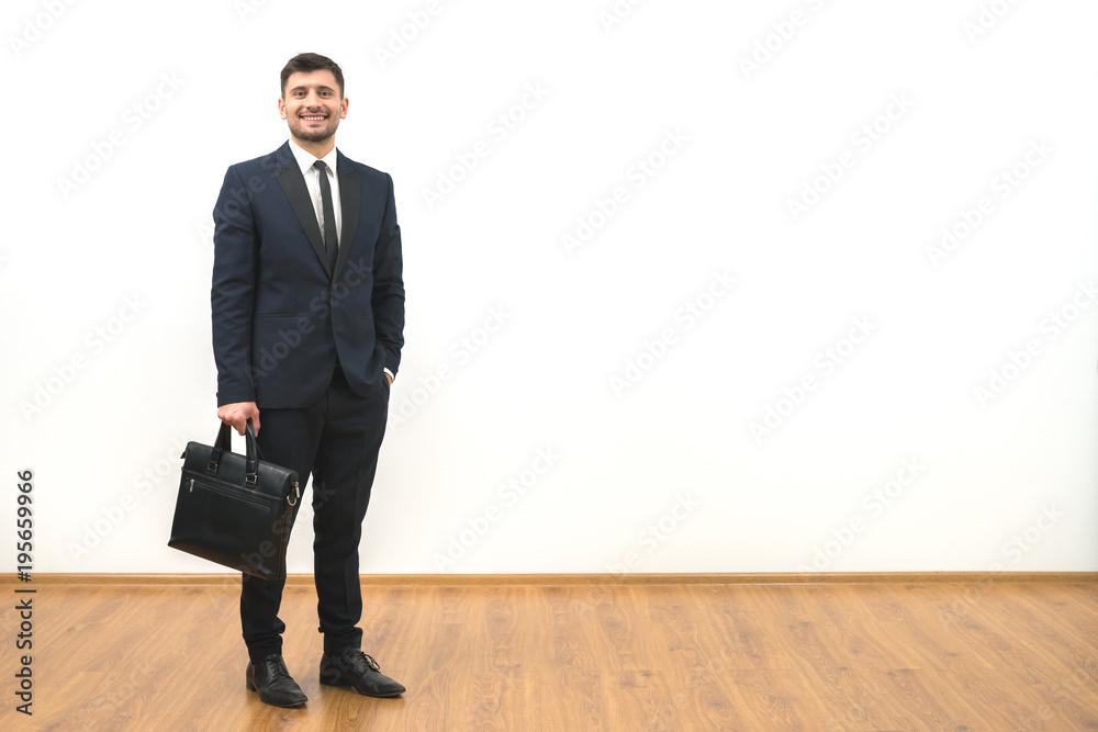 The happy businessman with a briefcase standing on the white wall background The happy businessman with a briefcase standing on the white wall background