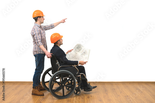 Slika na platnu The two engineers with a wheelchair gesture on the white wall background