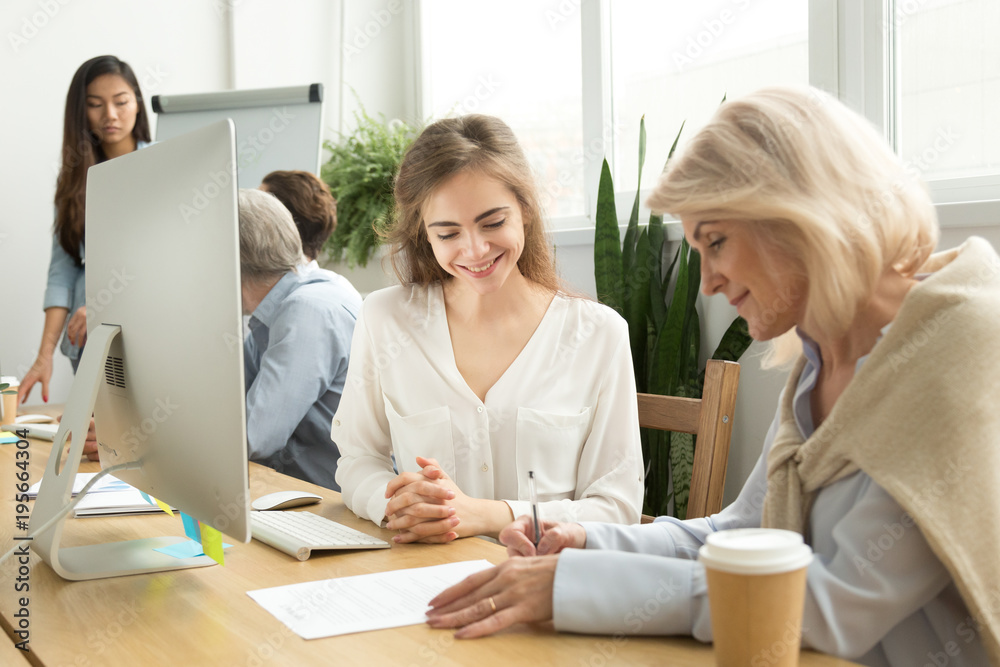 Older businesswoman signing paper contract with smiling female manager in coworking office, senior client putting signature on document making deal at meeting with advisor, taking loan insurance Older businesswoman signing paper contract with smiling female manager in coworking office, senior client putting signature on document making deal at meeting with advisor, taking loan insurance