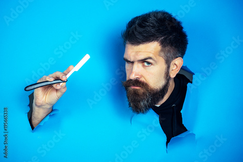 Barbershop concept. Bearded man look through paper. Serious bearded man holds razor. Barber shop for mens. Hairdressing equipment.
