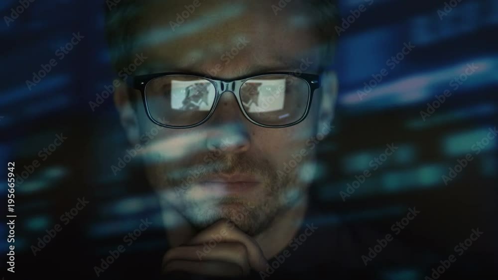 The serious man in glasses working near the screen. evening night time The serious man in glasses working near the screen. evening night time
