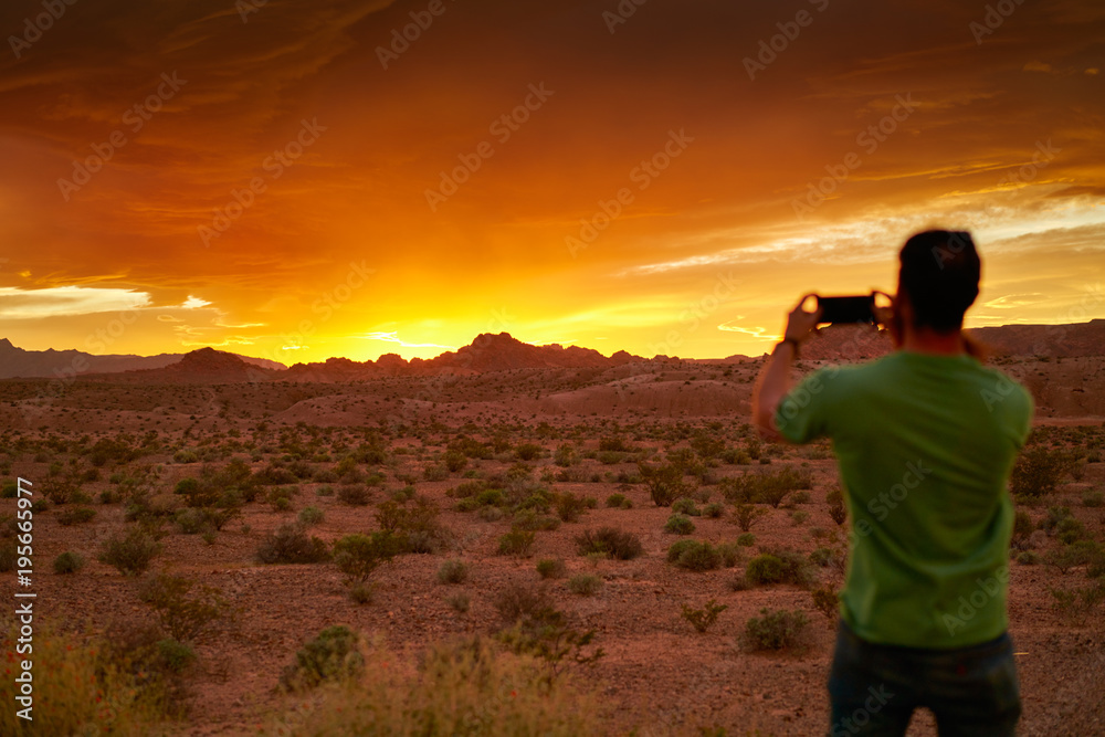 man taking photo with smartphone of very colorful sunset in nevada desert