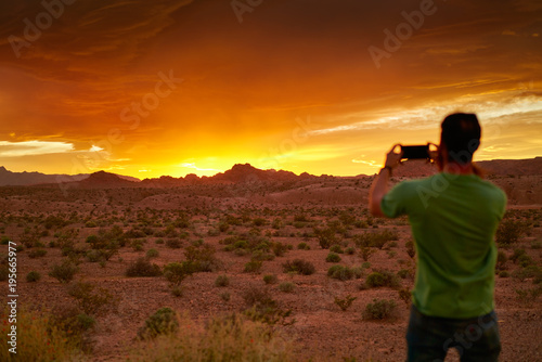man taking photo with smartphone of very colorful sunset in nevada desert © Joshua Resnick