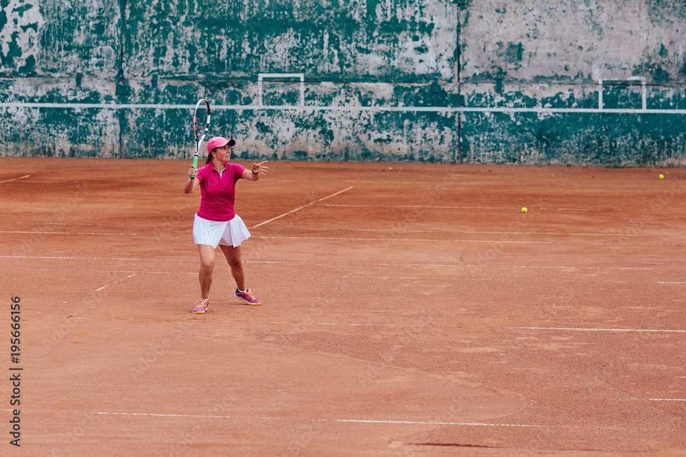 Tennis player. Athlete woman playing tennis, receiving a serve, dressed in pink t-shirt, cap and white skirt. Side view, on the court.