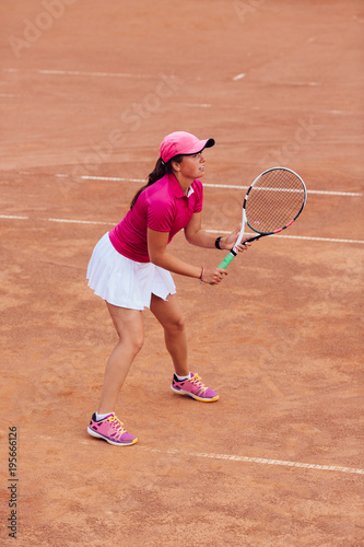 Tennis player. Outdoor photo of focused woman playing tennis on the court, dressed in pink t-shirt, cap and white skirt. Side view from tribune. © Maksym Azovtsev