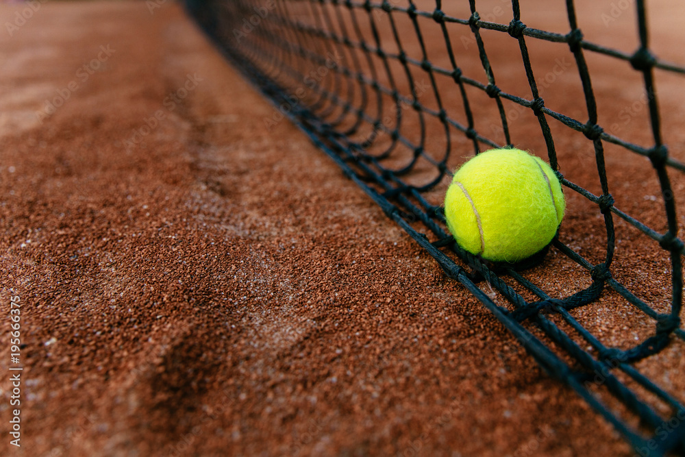 Close-up view of tennis ball near in the net, on artificial red tennis court.