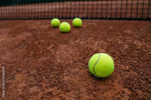 Close-up view of tennis balls near the net, on artificial red tennis court.