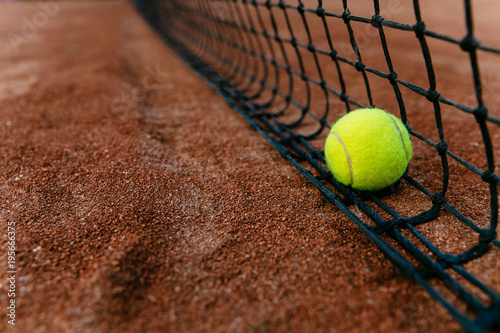 Close-up view of tennis ball near in the net, on artificial red tennis court. © Maksym Azovtsev