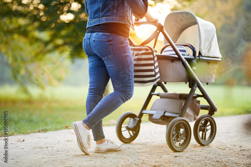 Woman with baby stroller walks in the park at sunset
