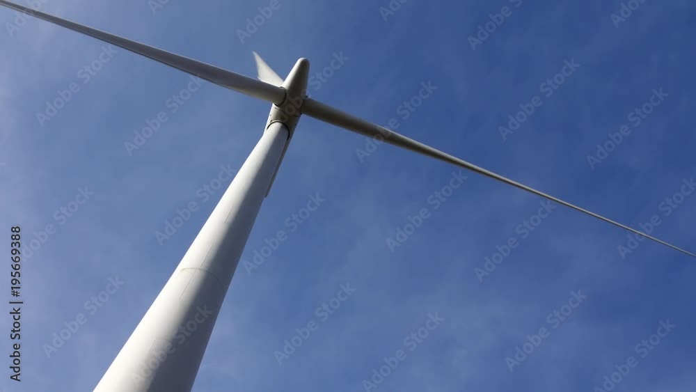 The turning blades of a wind turbine filmed from directly underneath. The turning blades of a wind turbine filmed from directly underneath.