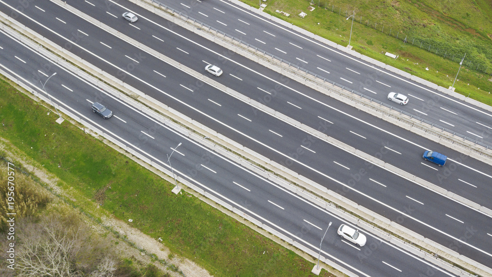 Aerial view of a stretch of highway in the Italian countryside. The road is divided into many lanes in each direction. There are cars and trucks on the street.Around the road there are trees and grass Aerial view of a stretch of highway in the Italian countryside. The road is divided into many lanes in each direction. There are cars and trucks on the street.Around the road there are trees and grass