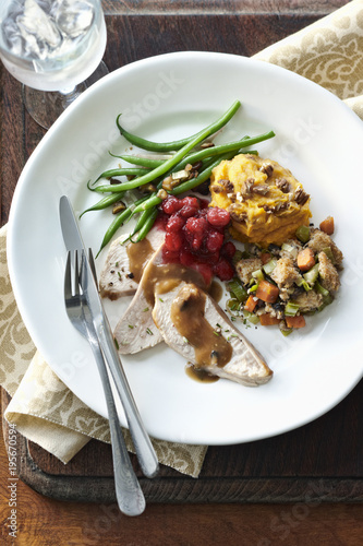 Holiday dinner plate with turkey breast, gravy, stuffing, sweet potato, green beans and cranberries on tabletop