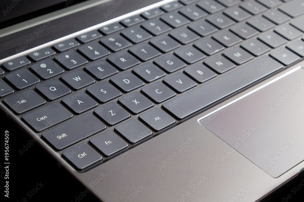 Part of opened laptop with keyboard, touchpad and empty mirror screen of black opened laptop isolated on black background side view closeup Part of opened laptop with keyboard, touchpad and empty mirror screen of black opened laptop isolated on black background side view closeup