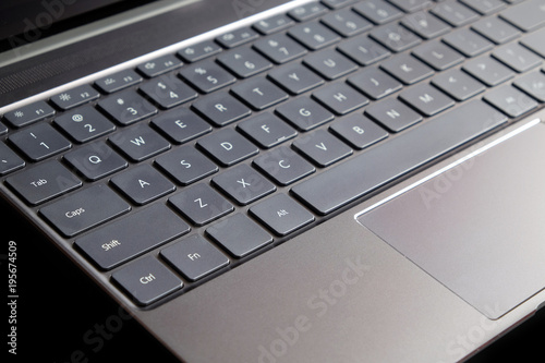 Part of opened laptop with keyboard, touchpad and empty mirror screen of black opened laptop isolated on black background side view closeup