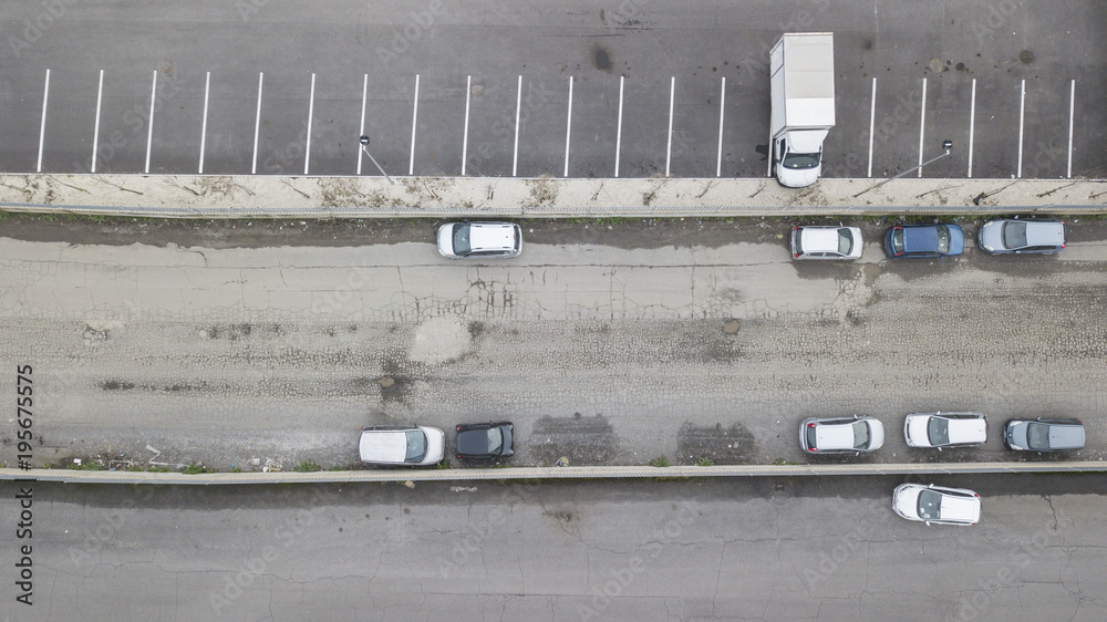 Perpendicular aerial view of a road. nobody is on the street. There are only a few cars and vans parked on the asphalt ruined by the holes.
