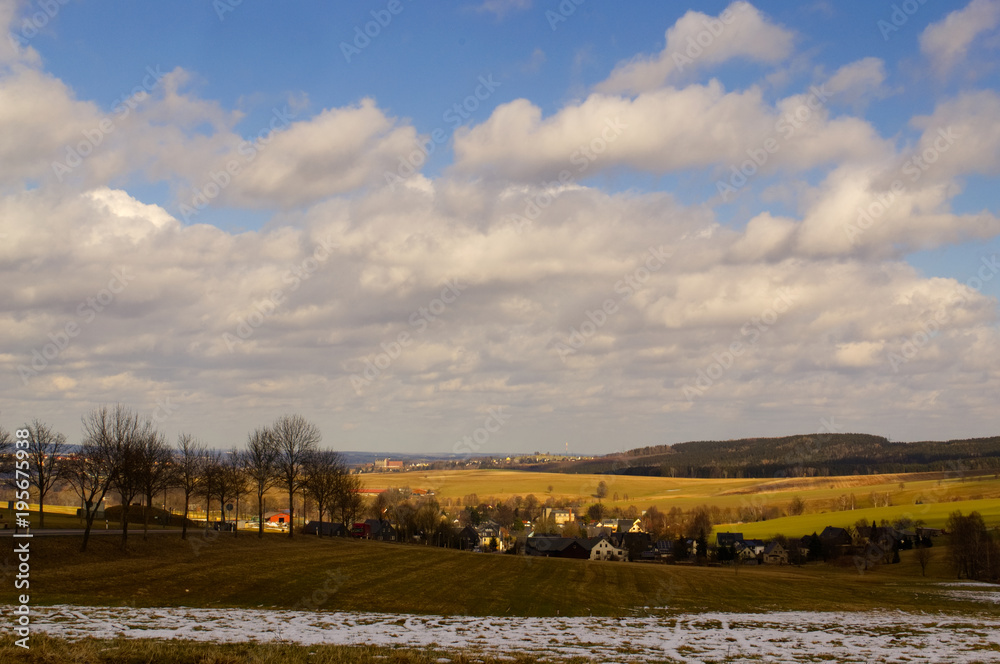 A landscape with forest, snow, meadows in springtime and a dramatic sky.