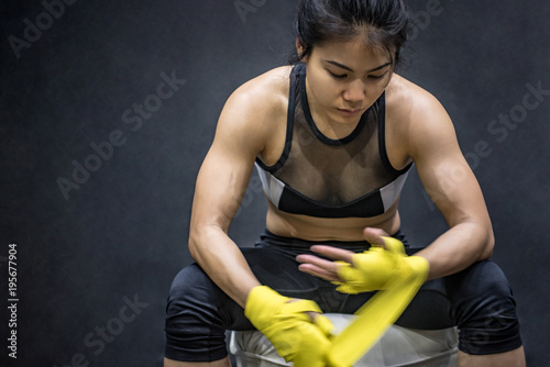 Asian female boxer wearing yellow strap on wrist. Beautiful young woman with muscular body preparing for boxing