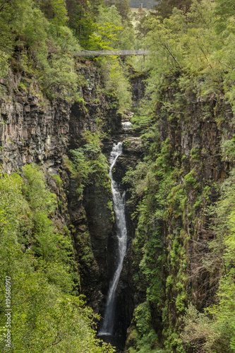 Braemore, Scotland - June 8, 2012: Corrieshalloch Gorge is a deep cut in landscape with forested vertical slopes with waterfall and a suspension bridge above.