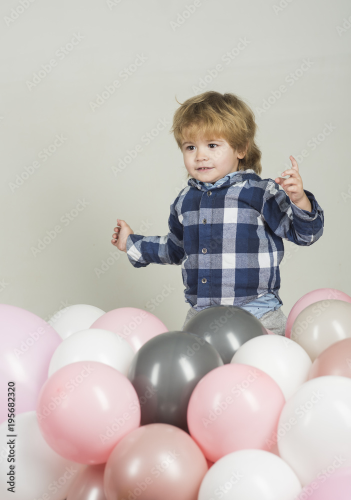 Little boy jumps in pink balloons. Funny kid play on his own on white background. Pink, white and gray balloons for celebration. Cute boy wearing blue shirt and grey jeans. Clothes for children Little boy jumps in pink balloons. Funny kid play on his own on white background. Pink, white and gray balloons for celebration. Cute boy wearing blue shirt and grey jeans. Clothes for children