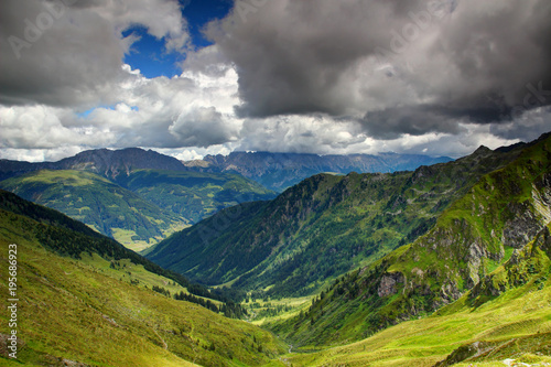 Sunny alpine meadows and forests in valleys of Karnische Alpen with ridges of Gailtaler Alpen   Lienzer Dolomiten in white cumulus clouds in background  Untertilliach Lesachtal Osttirol Austria Europe