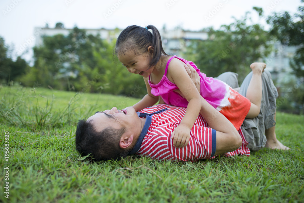 Asian man lying on lawn playing with his lovely little girl Asian man lying on lawn playing with his lovely little girl