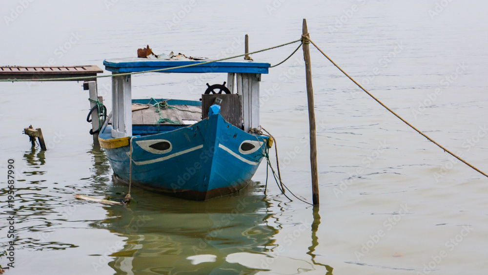 blue and white fishing boat  tied up at a pier on the river in Hoi An, Vietnam