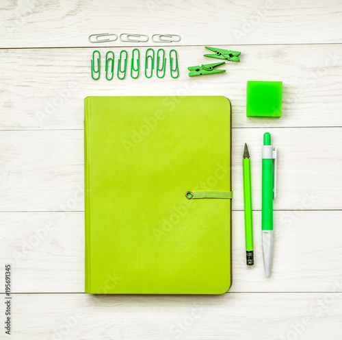 green notebook with eraser, pen,pencil and paper clips on white wooden background. creative set for dreawing,writing or making notes photo