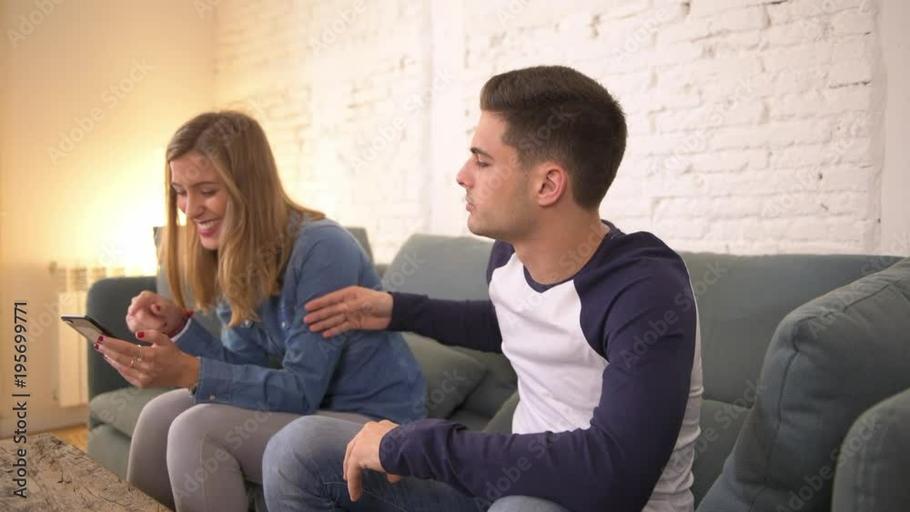 panning shot of young woman using social media on mobile phone ignoring her boyfriend at home sofa couch with the guy frustrated upset bored ignored by his girfriend in internet addict panning shot of young woman using social media on mobile phone ignoring her boyfriend at home sofa couch with the guy frustrated upset bored ignored by his girfriend in internet addict