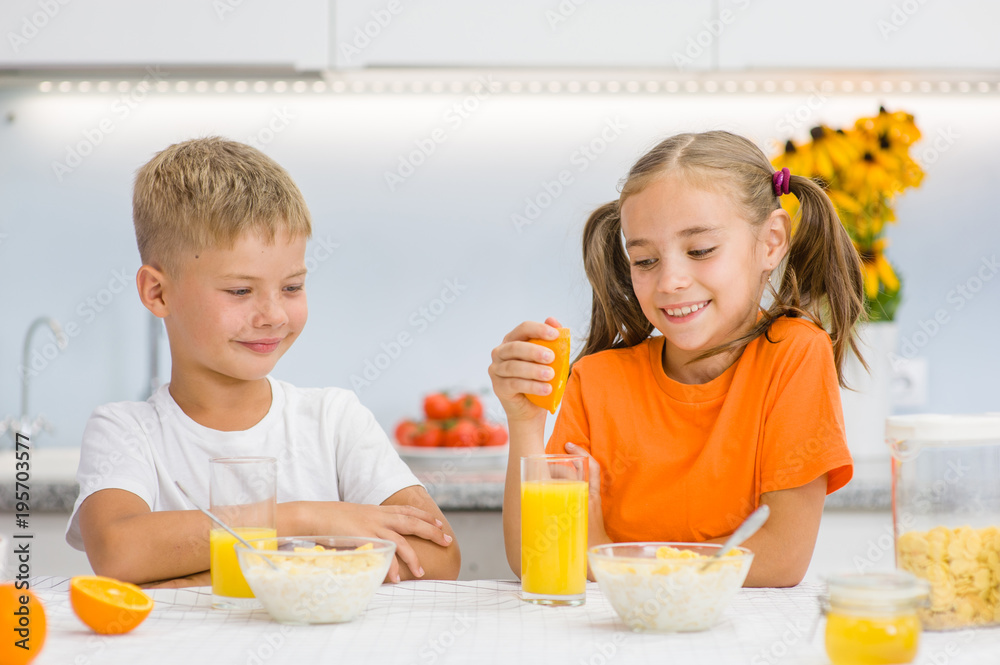 Happy girl squeezes orange juice to her brother for breakfast Happy girl squeezes orange juice to her brother for breakfast