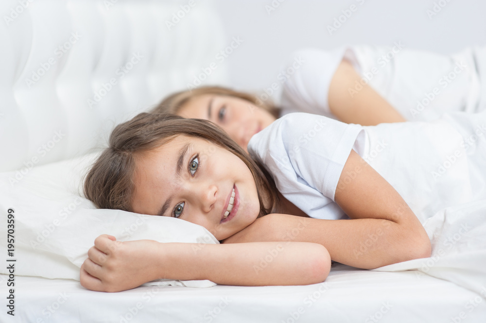 Happy little girl lying with sleeping mother on the bed in the bedroom Happy little girl lying with sleeping mother on the bed in the bedroom