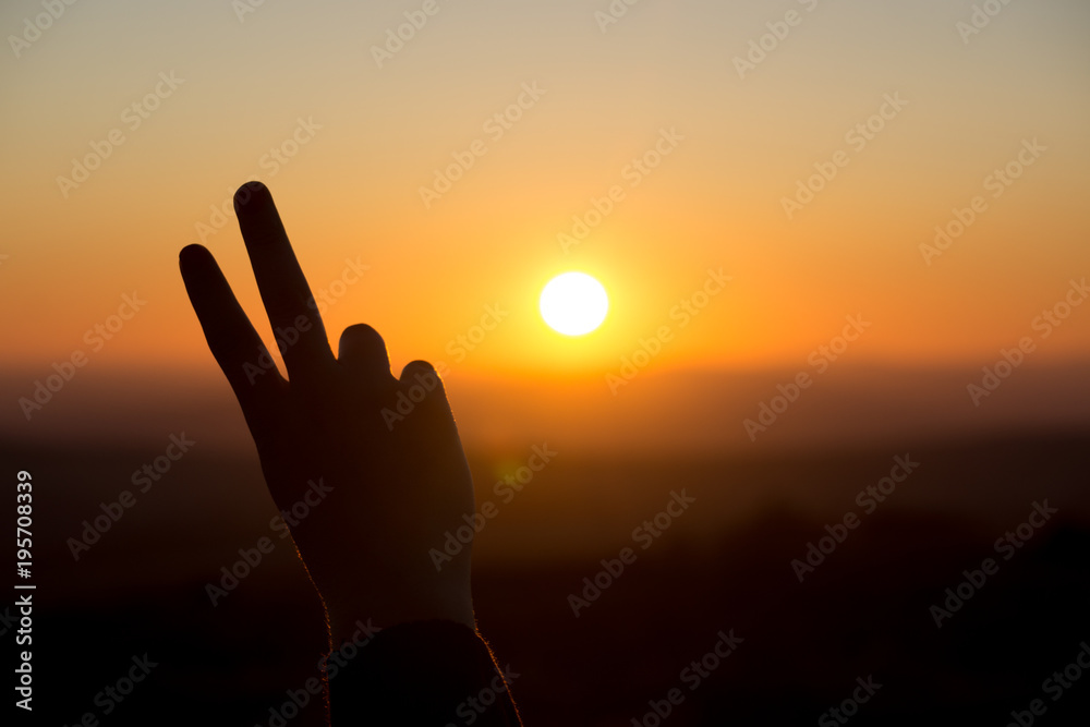 A peace sign hand gesture is silhouetted by the setting sun in Dartmoor, UK