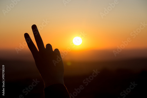 A peace sign hand gesture is silhouetted by the setting sun in Dartmoor, UK