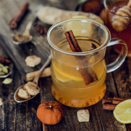Vitamin healing tea with lemon and honey, ginger and spices on wooden background in rustic style. The concept of spring beriberi and colds. Square image.