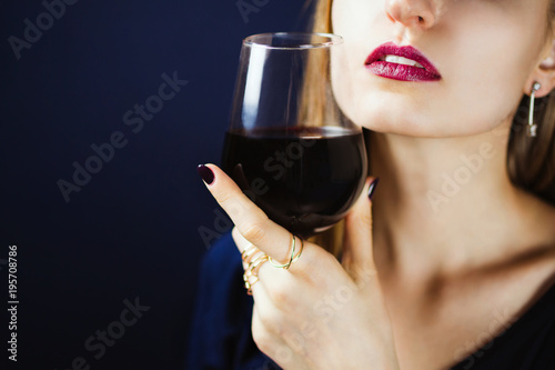 Faceless portrait of young adult white woman wearing dark plum lipstick holding a glass of red wine in her hand. Selective focus.