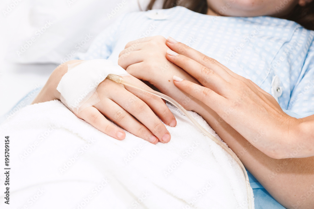 Mother holding little girl hand with IV saline intravenous in hospital