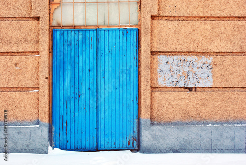 Closed blue painted door, pink plaster on wall, grunge background, winter snowy street, horizontal