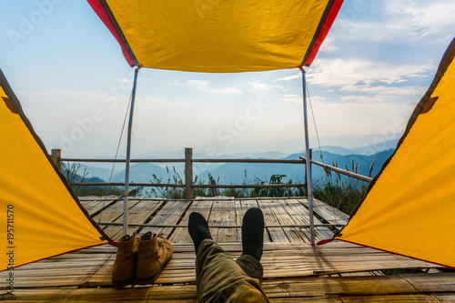 View from inside a tent at the forest and male legs emerge from tent.